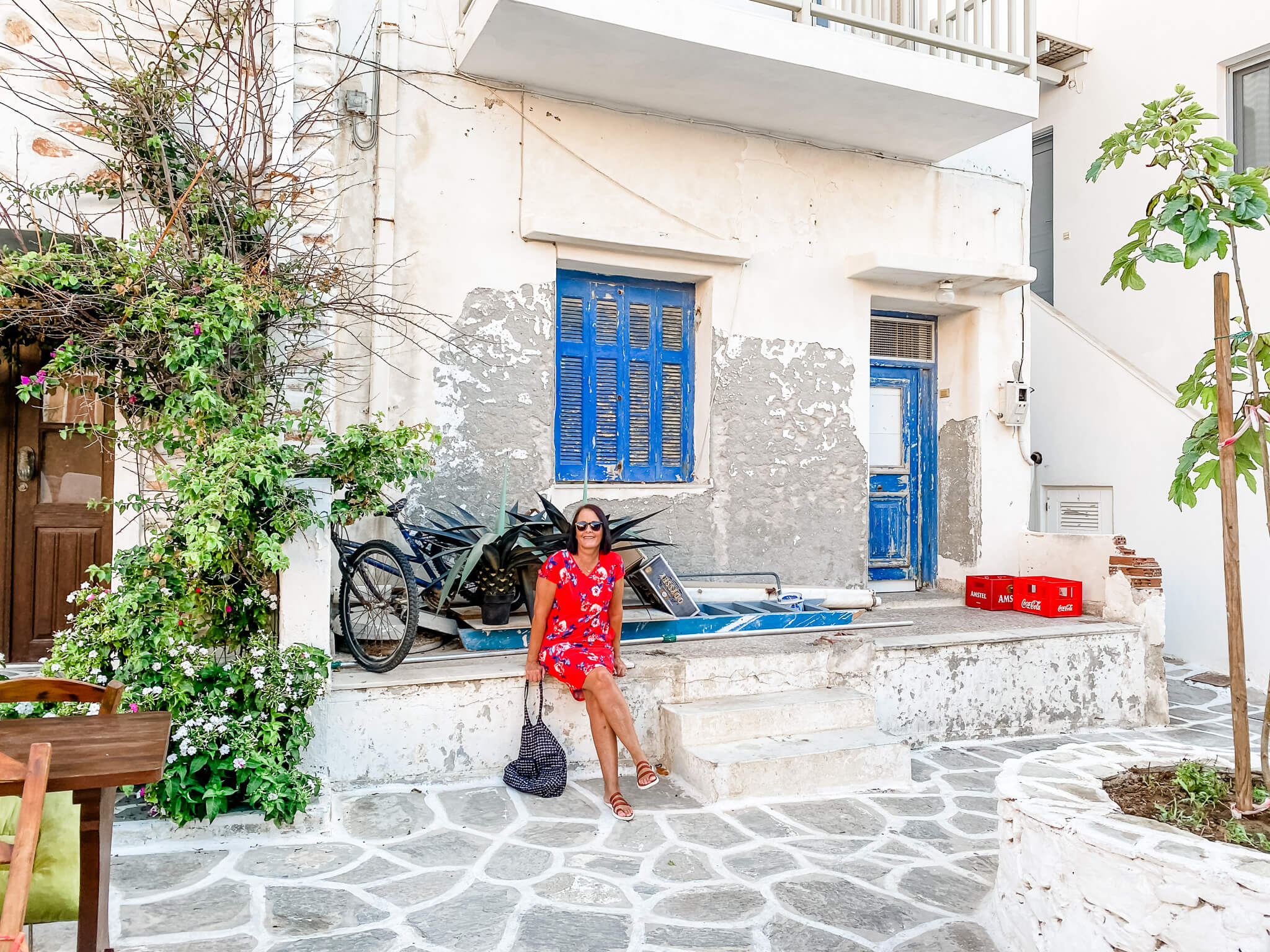 woman in red dress sitting in front of white building with blue shutters