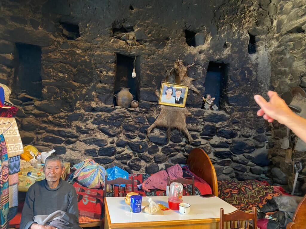 Inside of Rock House with man sitting with items to sell