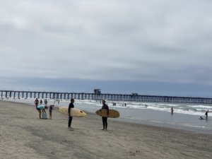 2 people holding surfboards in front of pier
