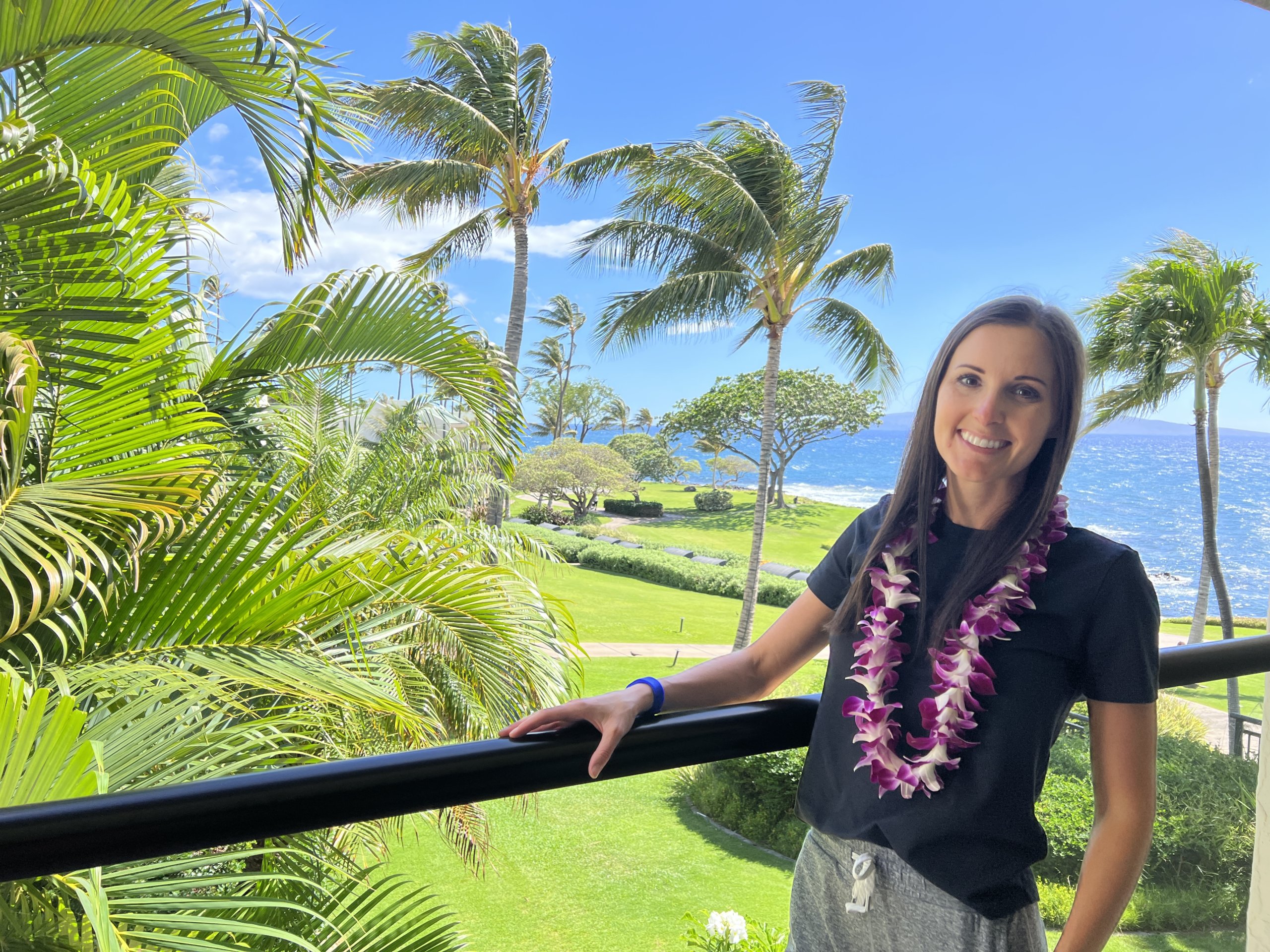 woman standing on balcony in front of palm trees and ocean
