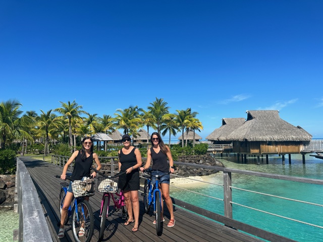 3 women on bikes in front of overwater bungalows