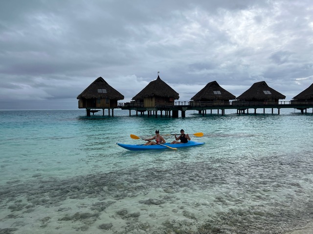 2 women kayaking in front of overwater villas