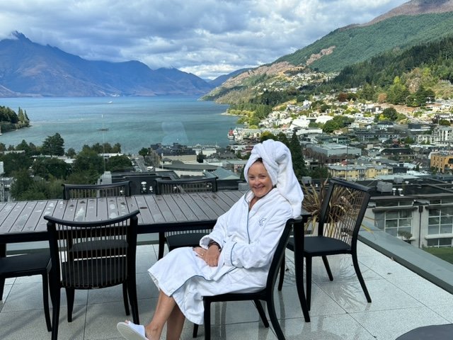 Woman in bathrobe on terrace in front of mountains and water