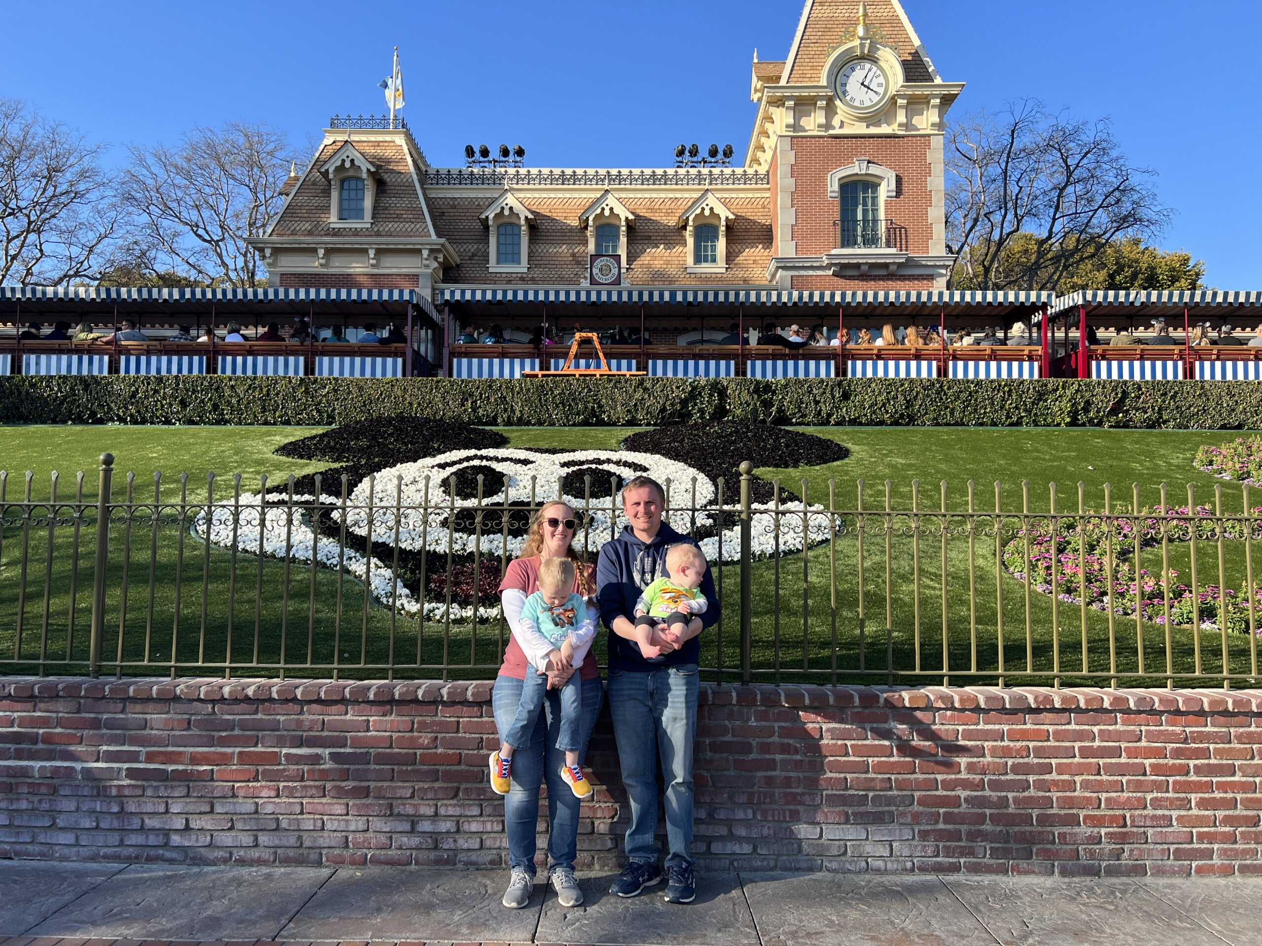 Man and woman holding children standing outside building with Mickey Mouse on lawn.