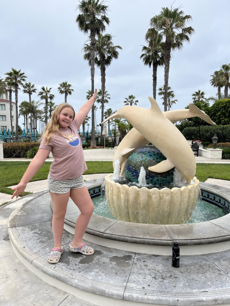 Girl standing by dolphin fountain.