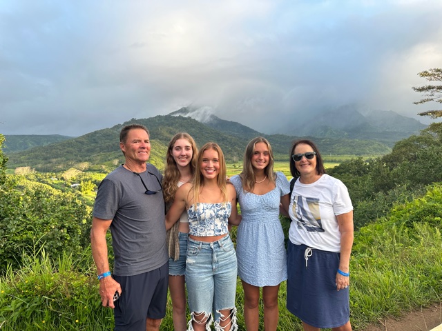 Picture of woman and man with three young girls overlooking green valley.