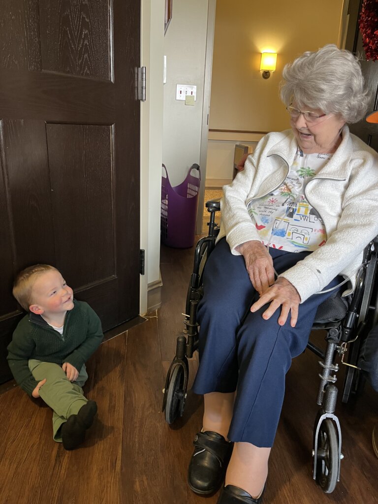 Older woman in wheelchair with young toddler on floor.