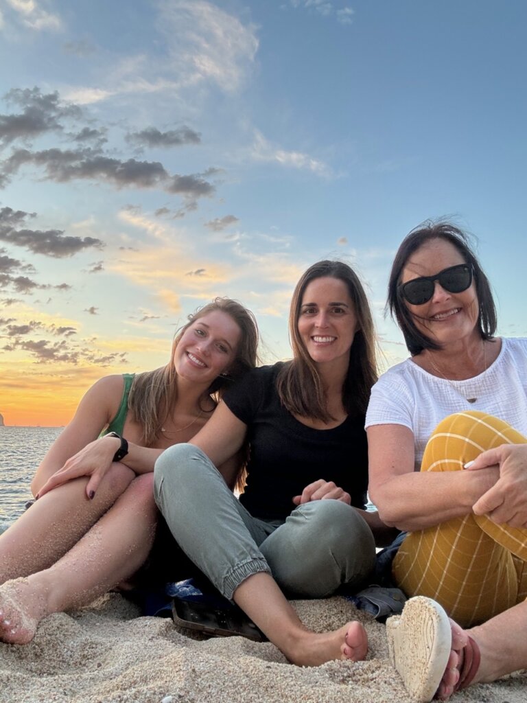 Three woman on a beach with a sunset in the back.