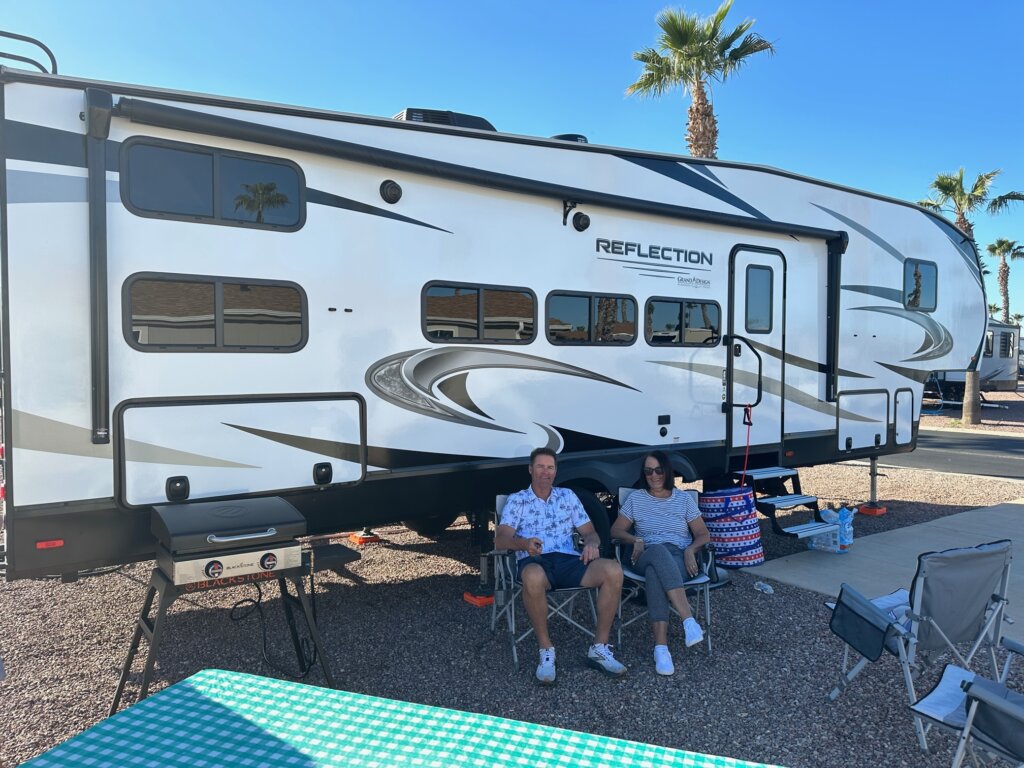 Couple sitting on chairs by fifth wheel trailer.