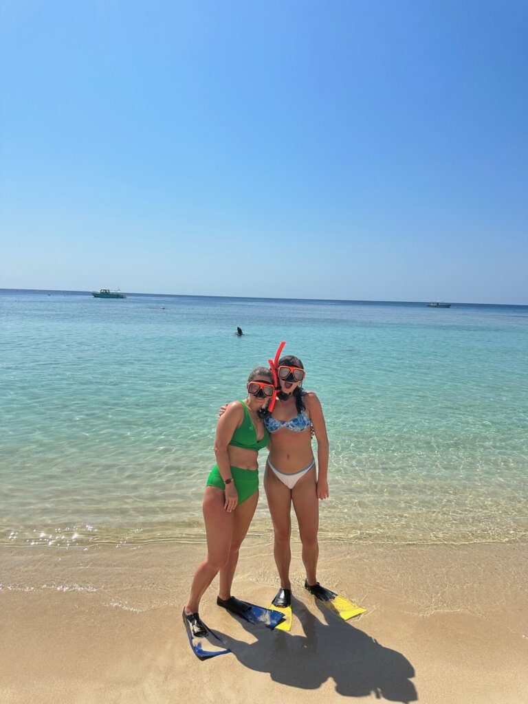 Two girls with snorkeling gear on near ocean.