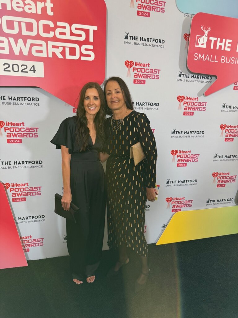 Two women standing in front of Iheart podcast award signs