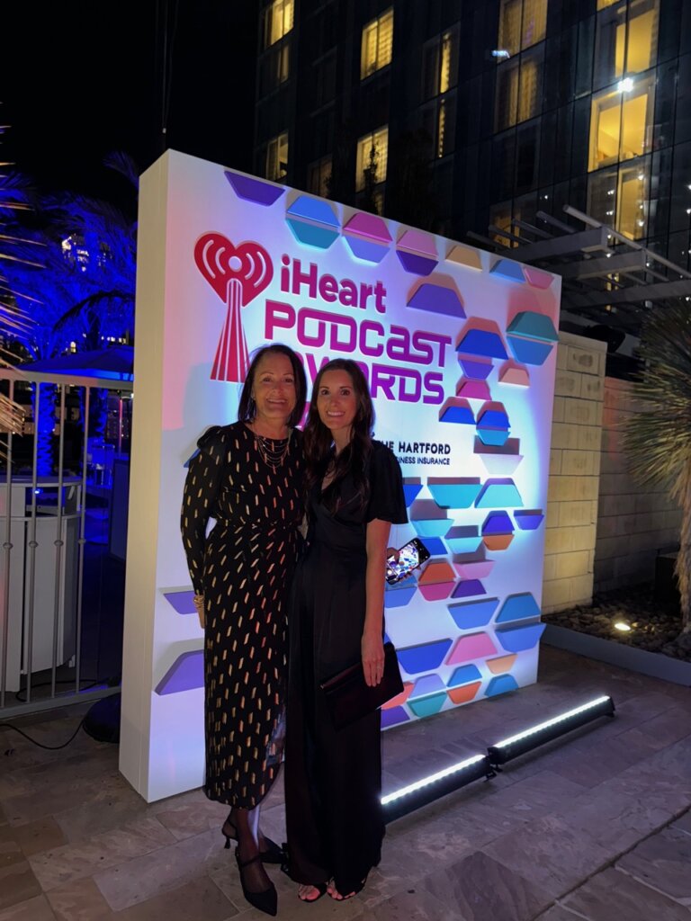 Two women standing in front of iheart radio podcast sign