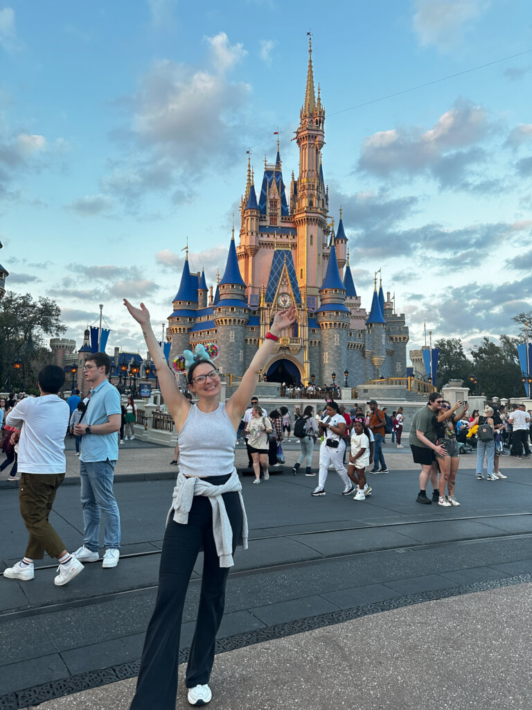 Woman standing with arms raised in front of a castle.