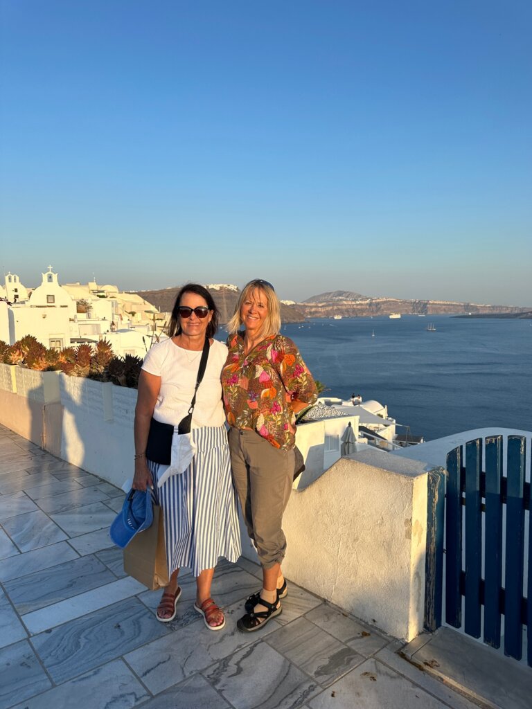 Two women standing in front of blue water and white buildings.