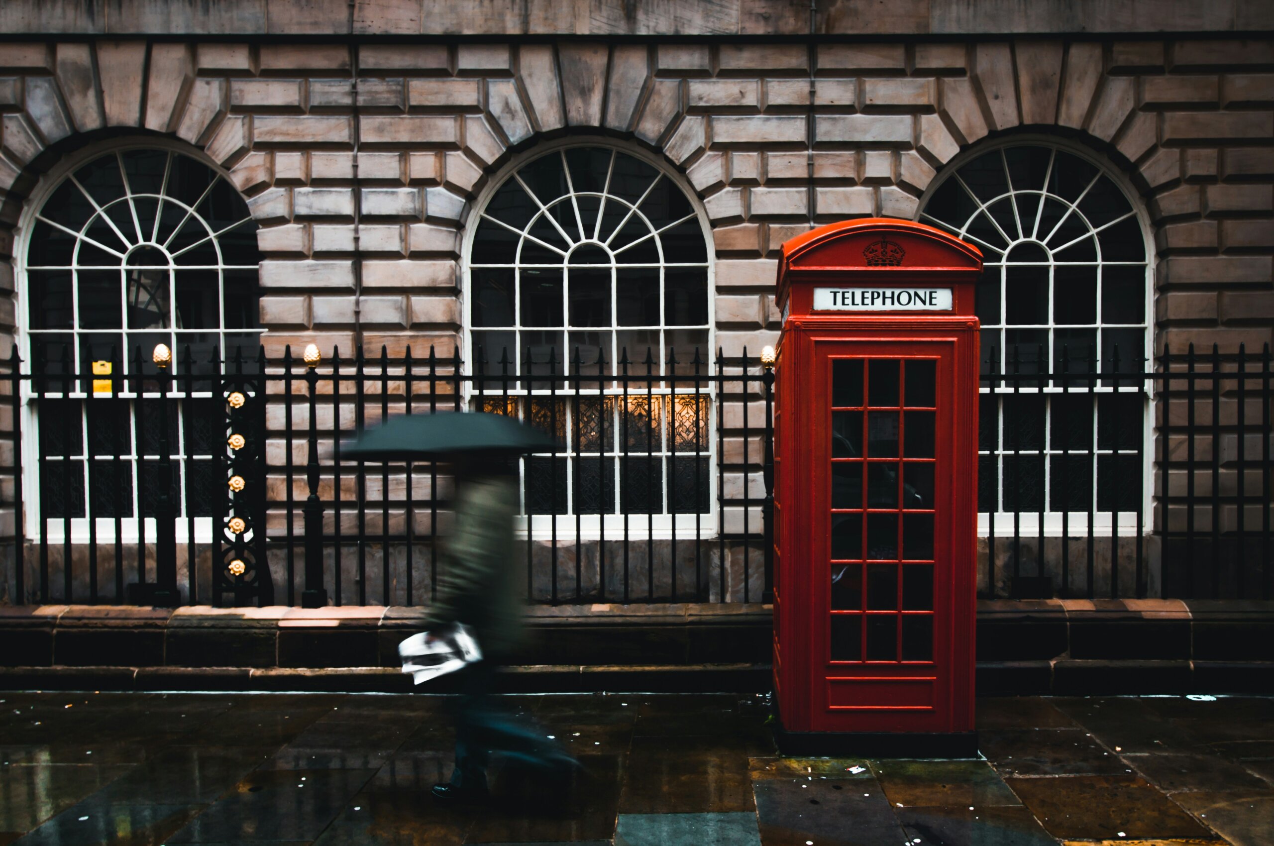 Red phone booth in front of building of bricks